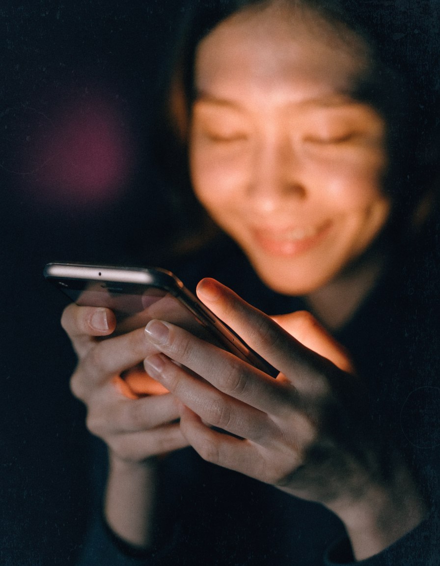 Manos escribiendo un mensaje en el celular, rostro iluminado en calido
